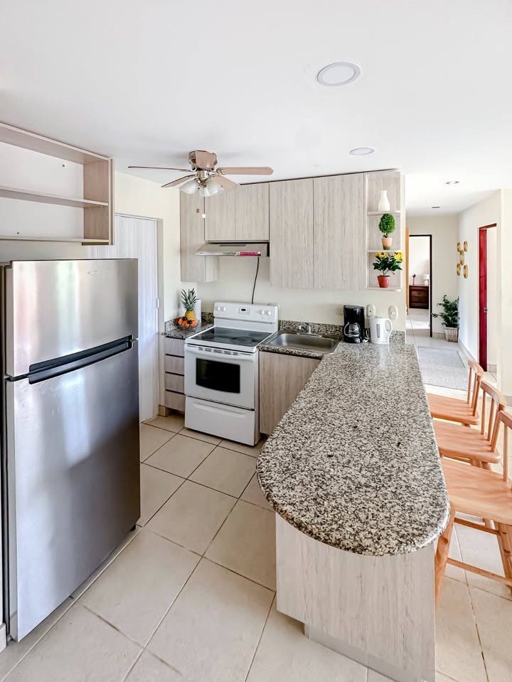 Kitchen with stainless fridge, electric stove and oven, granite breakfast bar with stools and a ceiling fan
