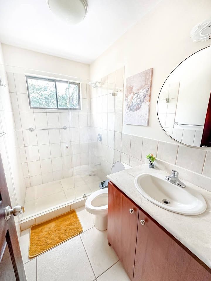 Bathroom with a glass walk-in shower, toilet, vanity sink with cabinet and a round mirror
