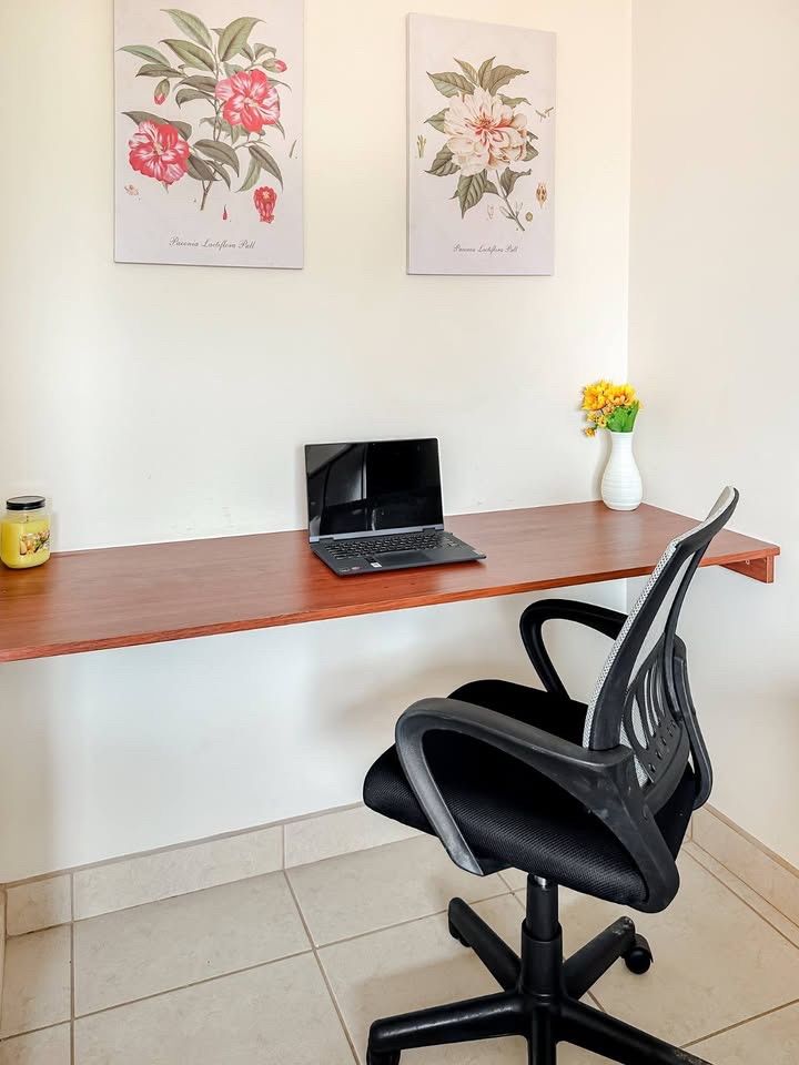 Wall-mounted wooden desk with a laptop and a black mesh office chair